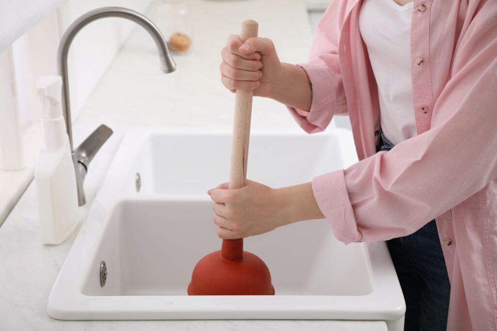 Hands working a kitchen sink with rubber drain plunger