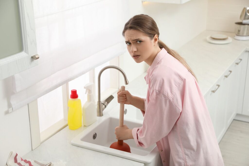 Worried girl trying to unclog sink with rubber drain plunger