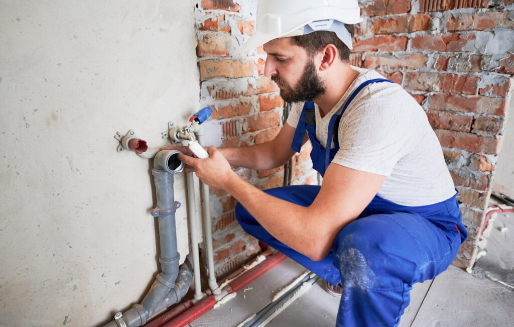 Plumber in a white safety hat fixing water pipes